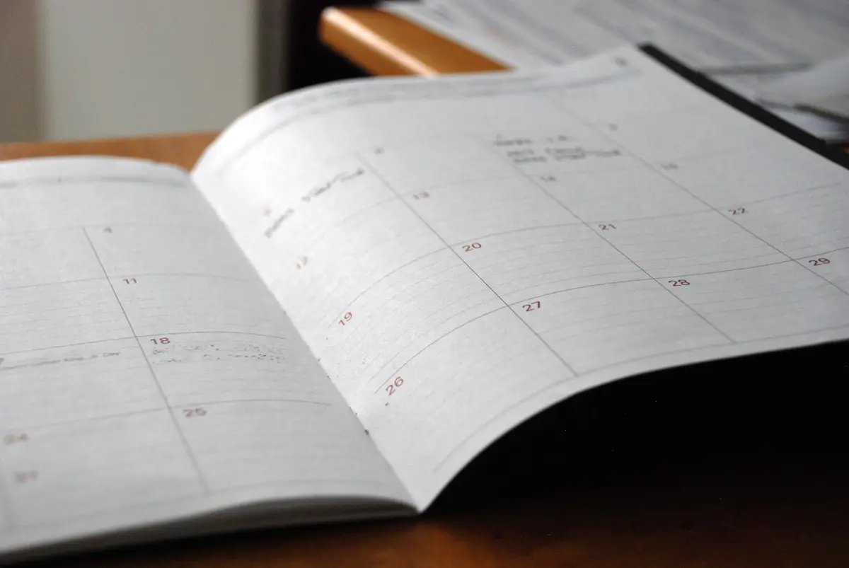 An open paper planner with a monthly calendar grid, lying on a wooden desk