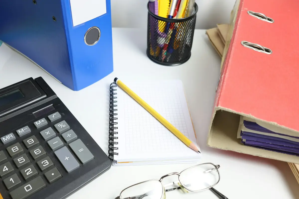 Desk with a calculator, binders, a notebook and reading glasses, set up for year-end tax paperwork